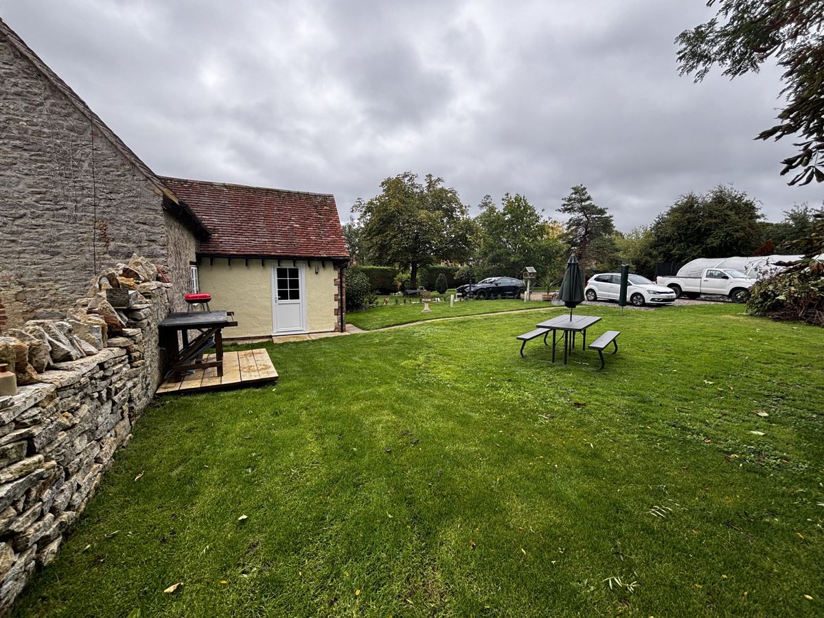 Lower Farm Cottage, a stone and cream-rendered cottage with a wide lawn and picnic bench